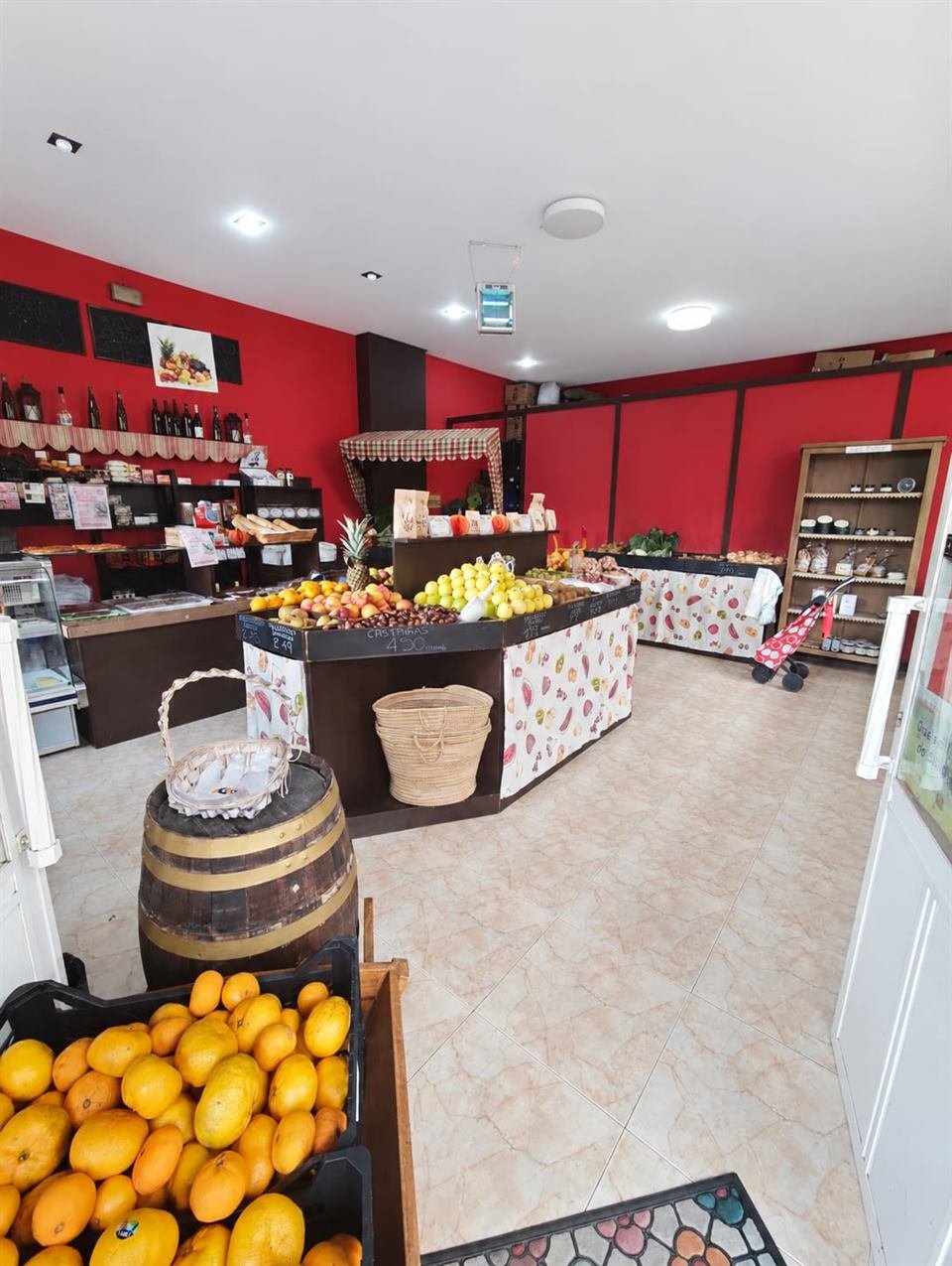 Interior de Froitas Améndoa: mostrador de fruta, estanterías con vinos y productos gourmet, y una caja de naranjas a la entrada